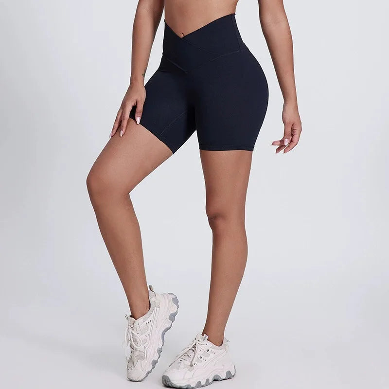 Person wearing black high-waisted shorts and white sneakers on a light gray background brand Gymelle