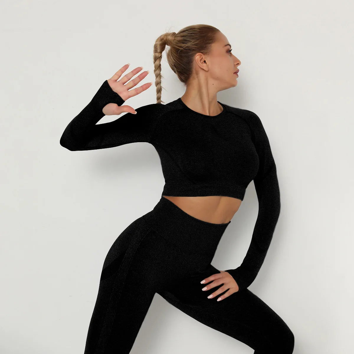 Woman wearing a black long-sleeve crop top and leggings against a light gray background