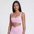Woman wearing a pink sports bra and leggings on a light gray background brand Gymelle